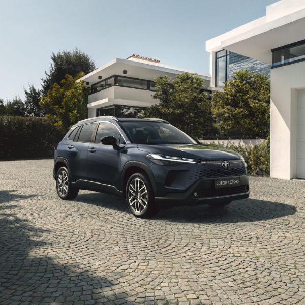 Tamsiai mėlynos spalvos Toyota automobilis stovi prie baltų namų.
