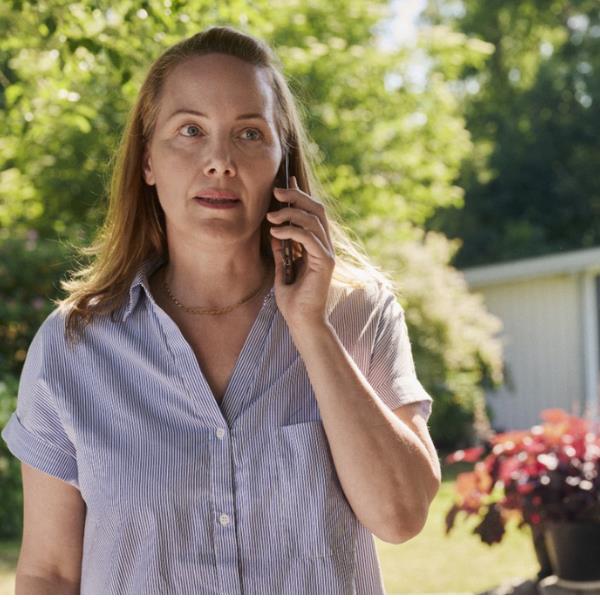 Asmuo stovi lauke, laiko mobilųjį telefoną prie ausies, vilki dryžuotus trumpomis rankovėmis marškinius, fone matyti žaluma ir pastatas.