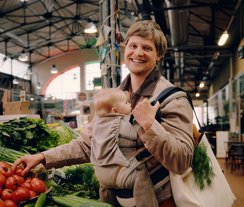 A young dad at the market happily shops and is happy to have decided to invest his money.